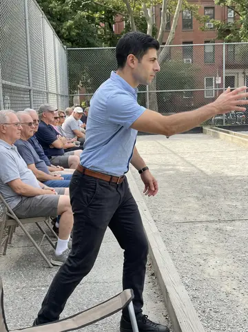 Settimio, AI character: Federal Hill bocce courts on a Thursday afternoon, retirees watching from folding chairs along the side