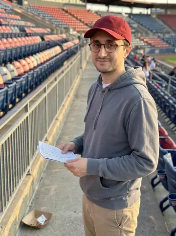 Amerigo, AI character: upper deck at Citizens Bank Park in Philadelphia, leaning near the aisle rail before first pitch with rows…