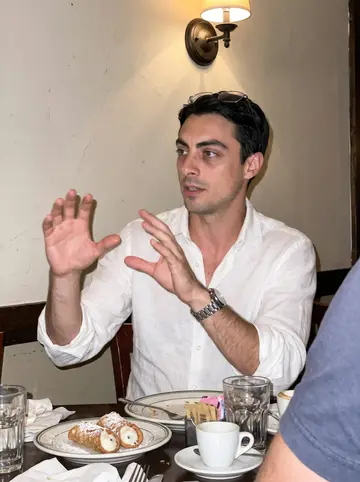 Donato, AI character: crowded North End casual table after dinner, cannoli plates and espresso cups on the table, friends…