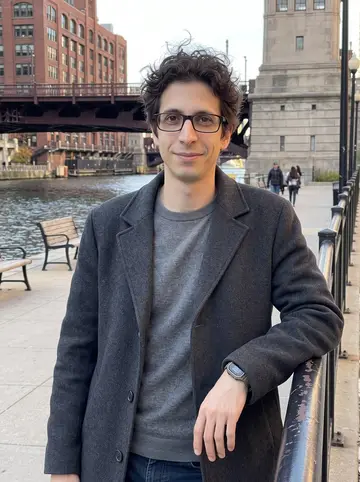 Mattias, AI character: Chicago Riverwalk near the bridges in late autumn, leaning against a black metal railing with the river…