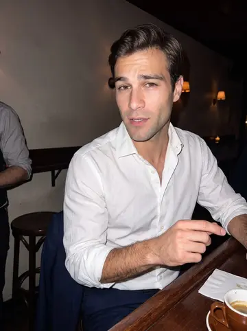 Gianluigi, AI character: a narrow Brooklyn bar where he is arguing grammar with a patient bartender, dark wood counter and…