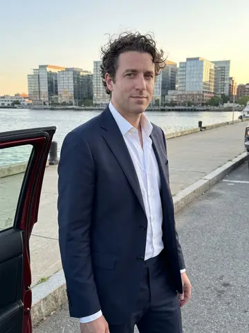 Pierpaolo, AI character: a quiet Boston waterfront parking lane near the Seaport at golden hour, standing beside the open door of a…