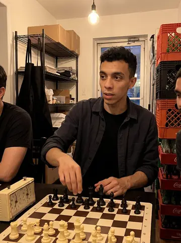 Lucio, AI character: after closing at the pizzeria, two coworkers and a chess board squeezed onto a small back table near…