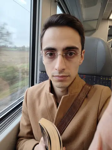 Raul, AI character: a regional train window seat between Bologna and a small client meeting outside the city, grey fields…