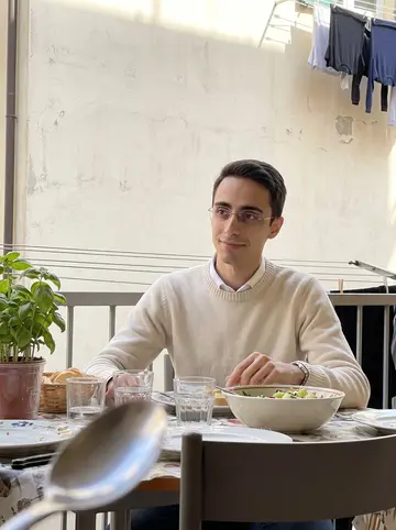 Raul, AI character: his mother's small apartment balcony in Bologna during a quiet Sunday lunch, laundry lines and potted…