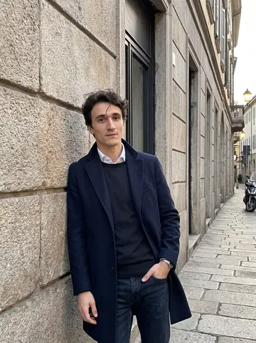 Silvio, AI character: a quiet side street in Brera, Milan, leaning against a stone wall outside a closed gallery after an early…