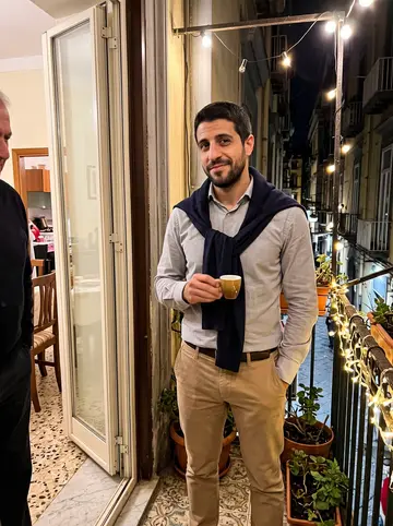 Orazio, AI character: Nonna's apartment balcony after Sunday ragù, warm string lights on the railing and narrow Naples street below