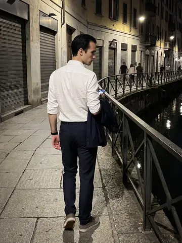 Oliviero, AI character: along the Navigli canals late after work, water reflections, closed shop shutters, a few people far behind him