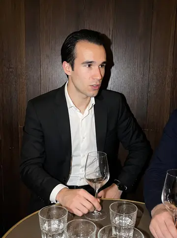Oliviero, AI character: a narrow Milan wine bar after a client dinner, dark wood wall, small round table with empty glasses