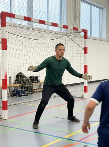 Rodrigo, AI character: indoor futsal court in a community sports hall in Denver on a Sunday late morning, his parka on the bench…