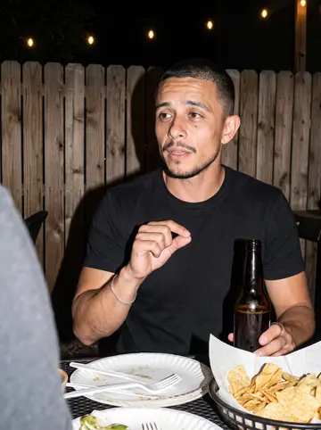 Rodrigo, AI character: back patio of a taqueria in Denver at night, a coworker's birthday table with paper plates, a bottle of…