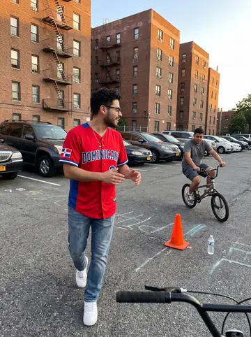 Moisés, AI character: the parking lot behind his Washington Heights building, chalk marks on the asphalt and a small bike beside…