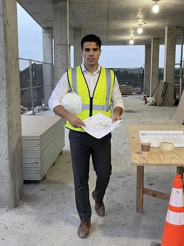 Tomás, AI character: a half-finished Miami construction site before sunrise, concrete columns, safety fencing, and a paper cup…
