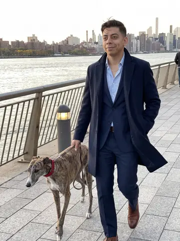 Fernando, AI character: the East River path near Gantry Plaza at dusk, Queens skyline and water behind him, Reina walking beside…