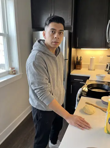 Fernando, AI character: his apartment kitchen on a Sunday morning in Jackson Heights, arepa dough bowl and cast-iron pan on the…