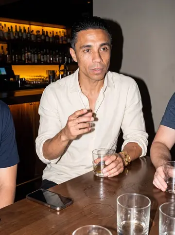 Marco, AI character: a small Las Vegas lounge after midnight, old merengue playing low and friends cropped around the edge of…