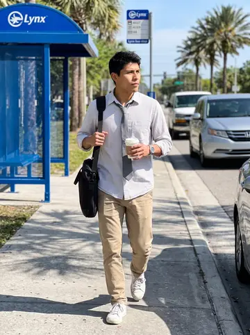 Efraín, AI character: sidewalk near a Lynx bus stop on his morning route through Orlando, palm trees and traffic in the background