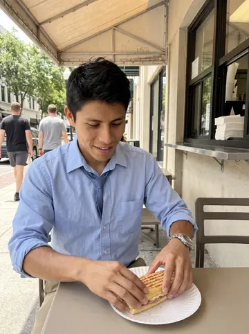 Efraín, AI character: outside a downtown Orlando Cuban sandwich window during his lunch break, plain awning shade and sidewalk…