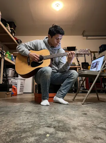 Efraín, AI character: family garage late at night, laptop open on a folding chair with a guitar tutorial paused, laundry shelves…