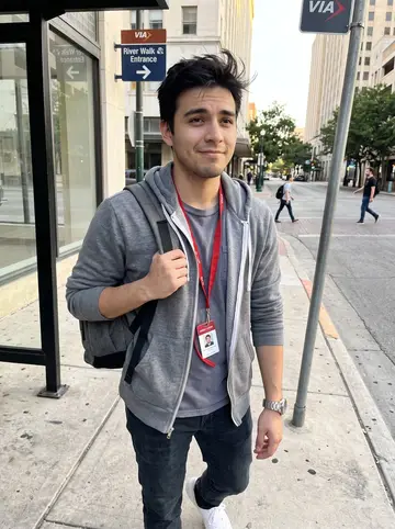 Humberto, AI character: downtown San Antonio near a VIA bus stop and a low sunlit street corner after class, the River Walk…