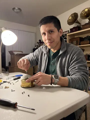 Benjamín, AI character: his new Albuquerque apartment, a folding table under a lamp with tiny screwdrivers, a headlamp, and…