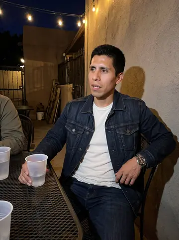 Benjamín, AI character: a low-key brewery patio in Albuquerque after work, string lights, plastic cups and a metal table, friends…