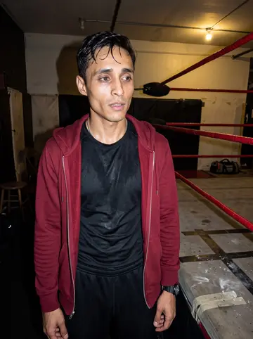 Joaquín, AI character: a West Side lucha libre gym after Saturday training, beside red ring ropes and scuffed mats