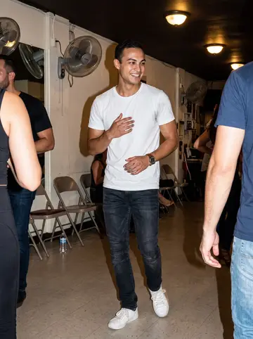 Armando, AI character: beginner salsa class in a Little Havana community dance room, standing in the back row near the wall fans