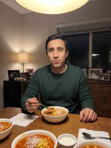Ulises, AI character: his tía's dining room on a rainy winter night, bowls of pozole, napkins, and family photos on a sideboard…