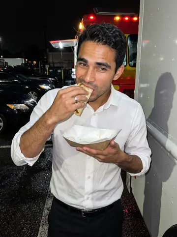Alejandro, AI character: a late-night taco truck parking lot after a summer monsoon shower, wet asphalt reflecting truck lights