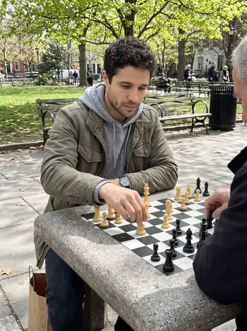 Yasser, AI character: an outdoor chess table in Rittenhouse Square, sitting across from an older man with the board between them