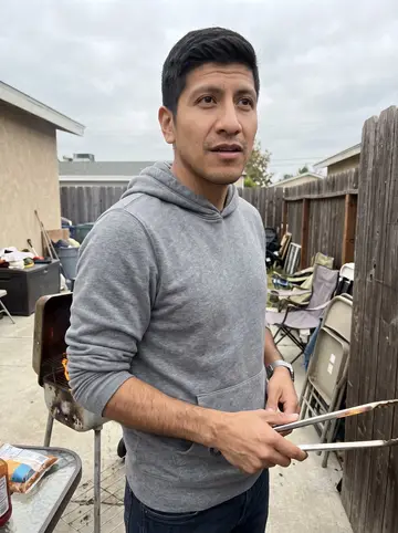 Ismael, AI character: a modest backyard cookout in Chula Vista, folding chairs and a small grill under an overcast sky