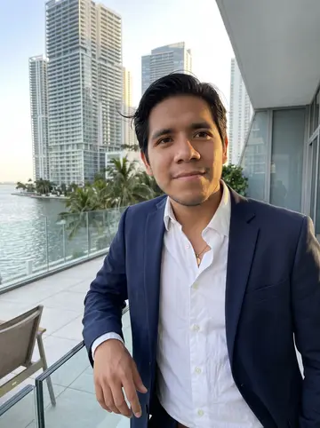 Maximiliano, AI character: a Brickell waterfront terrace in Miami at golden hour, glass towers and the bay soft behind him