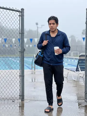 Maximiliano, AI character: outside a public lap pool in Miami just after dawn, wet pavement and lane ropes visible through the fence