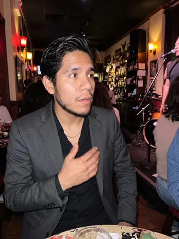 Maximiliano, AI character: a crowded Little Havana salsa bar, colored lights on the wall and a small live band partly visible behind him