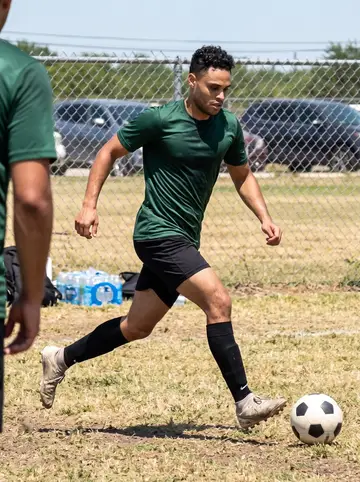 Wilfredo, AI character: a public soccer field on a Sunday morning in San Antonio, dry grass and chain-link fence in the background