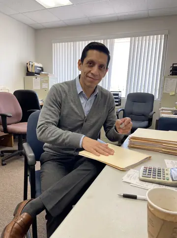 Arturo, AI character: the break table in his small Phoenix tax-prep office, manila folders and a calculator on the table