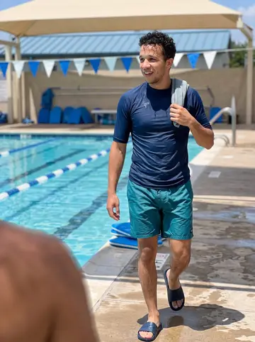 João, AI character: a public community pool in Austin after an adult swim lesson, with lane ropes and blue kickboards stacked…