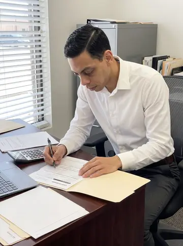 Thales, AI character: his small mortgage office near downtown Albuquerque, blinds half open, desk with a laptop, calculator and…