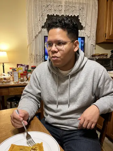 Erick, AI character: his abuela's apartment kitchen during a winter evening telenovela watch, lace curtain and old dining table…