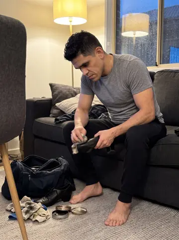 Yadiel, AI character: his apartment living room on a rainy Friday night, dance shoes, polish cloth, and a gym bag laid out by…