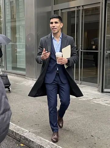 Brayan, AI character: outside a Midtown office tower during a late coffee run, wet sidewalk and glass doors behind him