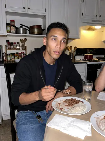 Yandel, AI character: a crowded Dominican kitchen in Providence on a Sunday night, plates of rice and beans on the table