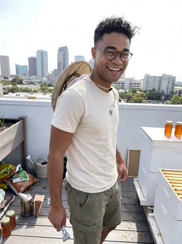 Raydel, AI character: a sunny Tampa rooftop garden beside white beehive boxes, downtown buildings soft behind him