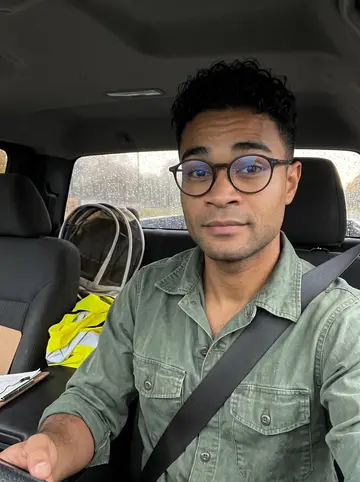 Raydel, AI character: parked in his work truck after a rainy drive, beekeeper veil and a folded safety vest on the passenger seat
