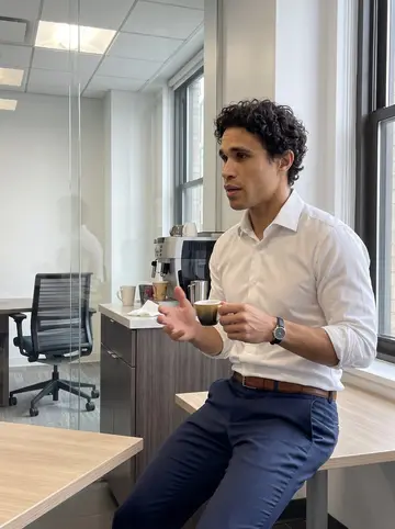 Vinícius, AI character: small pantry area beside a Midtown consulting office, espresso machine on the counter, glass meeting rooms…