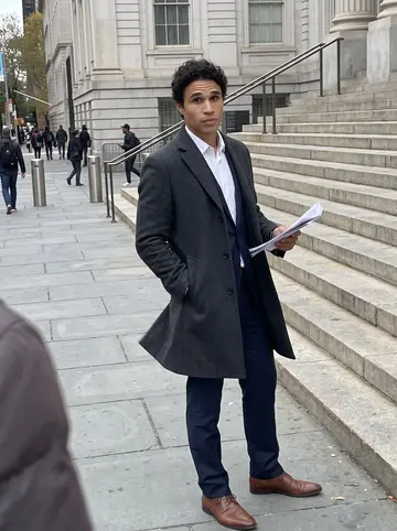 Vinícius, AI character: outside New York City Hall after an evening public hearing, stone steps and metal railings behind him