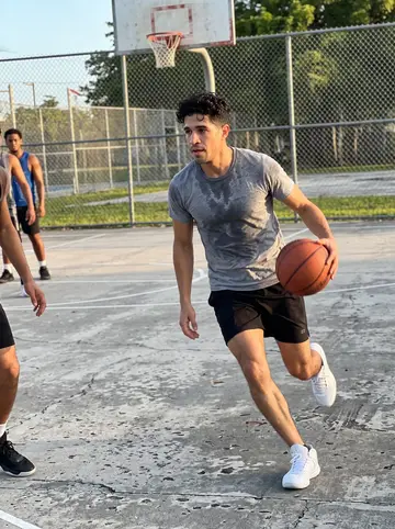 Ruairí, AI character: a Miami park basketball court with a cracked surface and an old backboard, early pickup game before shift