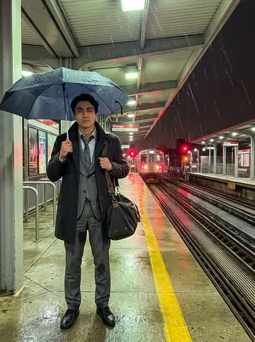 Dominik, AI character: Red Line platform in Chicago during a spring thunderstorm, wet concrete and train lights behind him