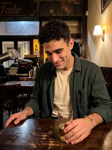 Vasco, AI character: a small fado bar in Porto on a rainy evening, dark wood tables and a tiny corner microphone behind him